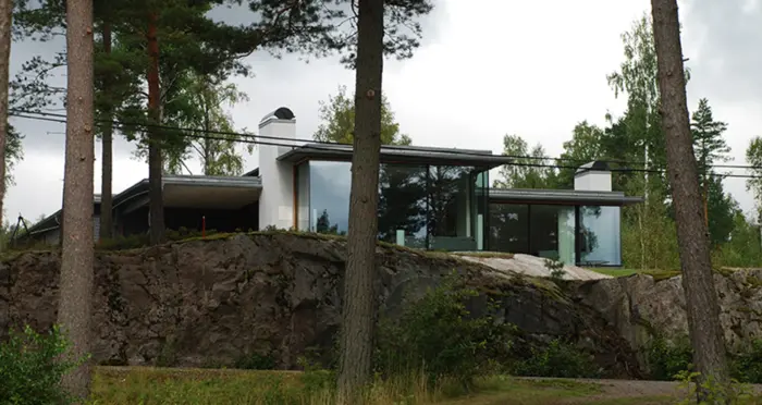 FÅG1 — boligen på bergknausen bak fjellskjæringen, med hvit pipe og store glassflater, mellom furuene