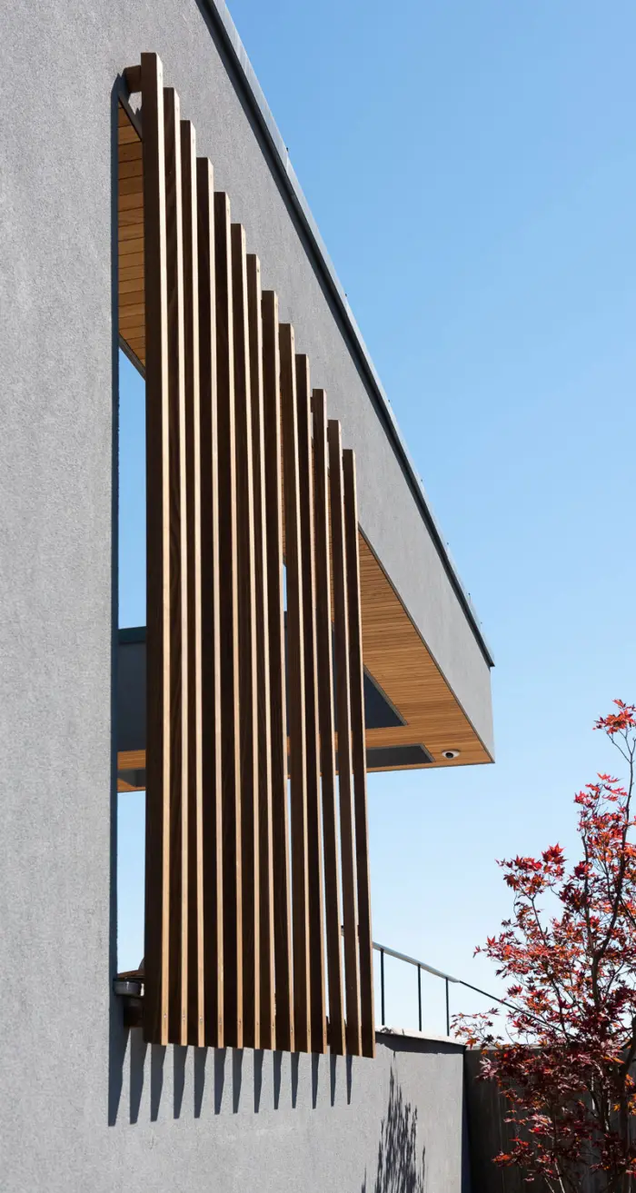 ÅSV28 — detalj av solskjerm i tre mot pusset grå vegg, under utkraget tak med undertak i tre