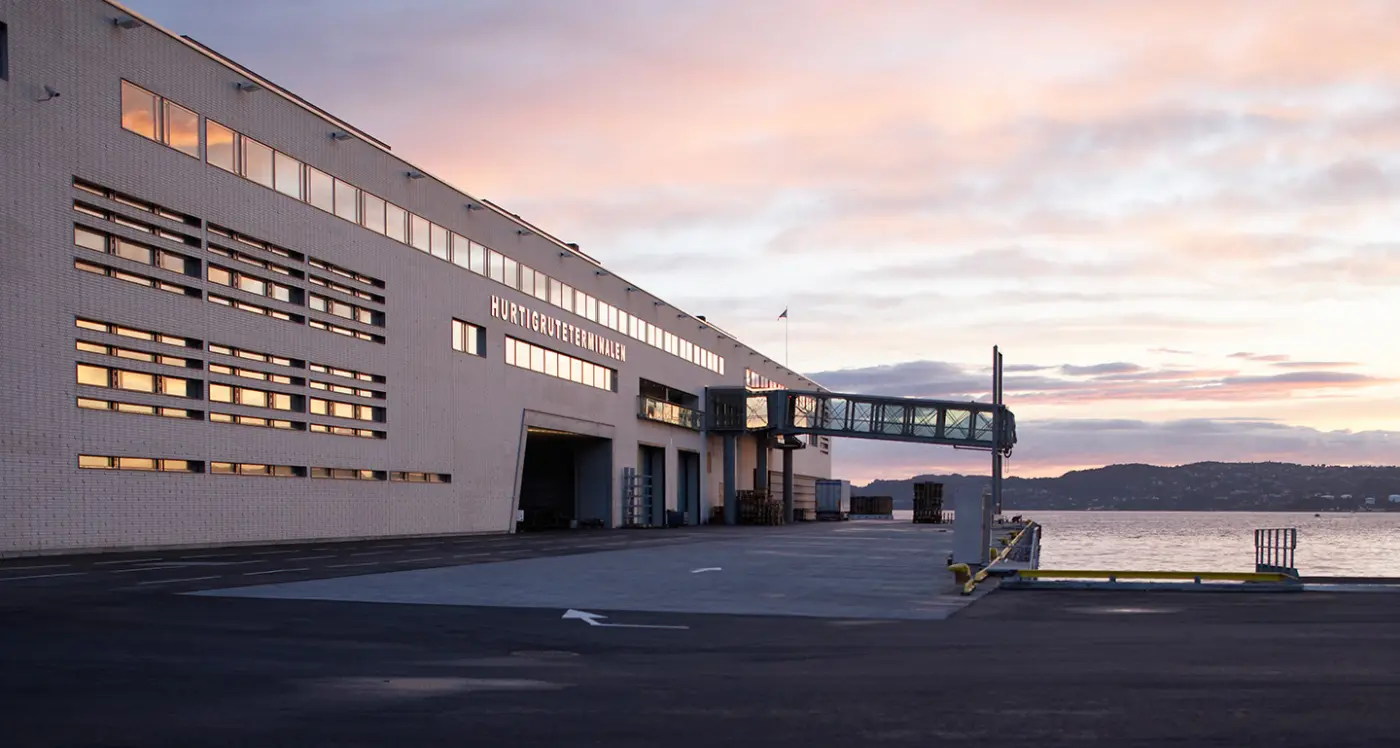 HRT — Hurtigruteterminalen i lys tegl med gangbro til kai, fotografert i solnedgang
