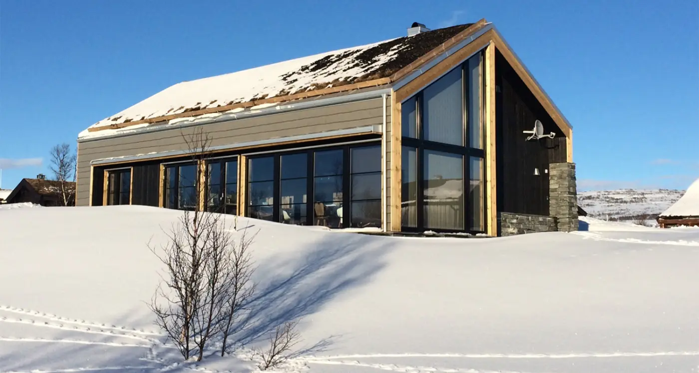 HOV — hytte med torvtak og glassfasade under høy gavl, med natursteinsmur, på snødekt fjell