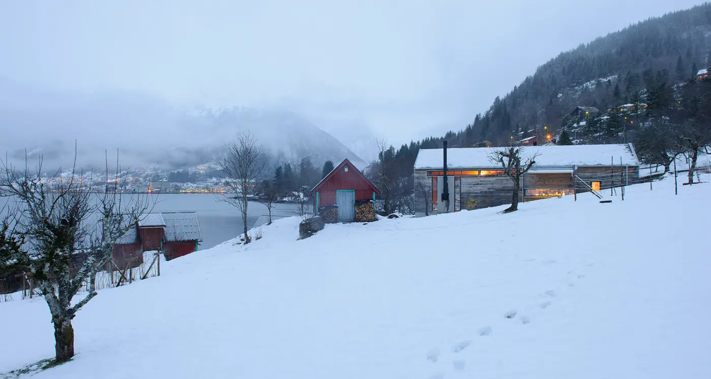 BAL — boligen i snølandskapet med opplyste vinduer, mellom eldre uthus ved fjorden