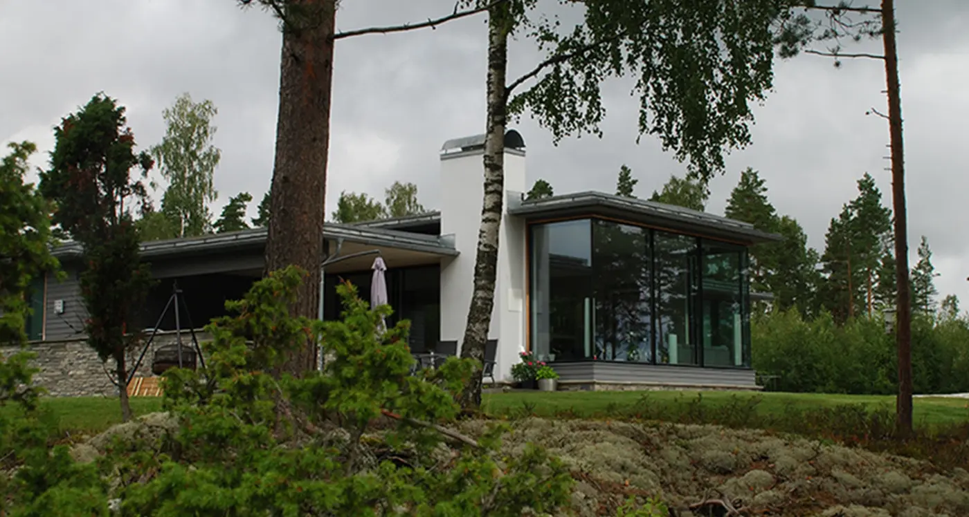 FÅG1 — hvit bolig med stort hjørnevindu og lavt tak, i furuskog med natursteinsmur