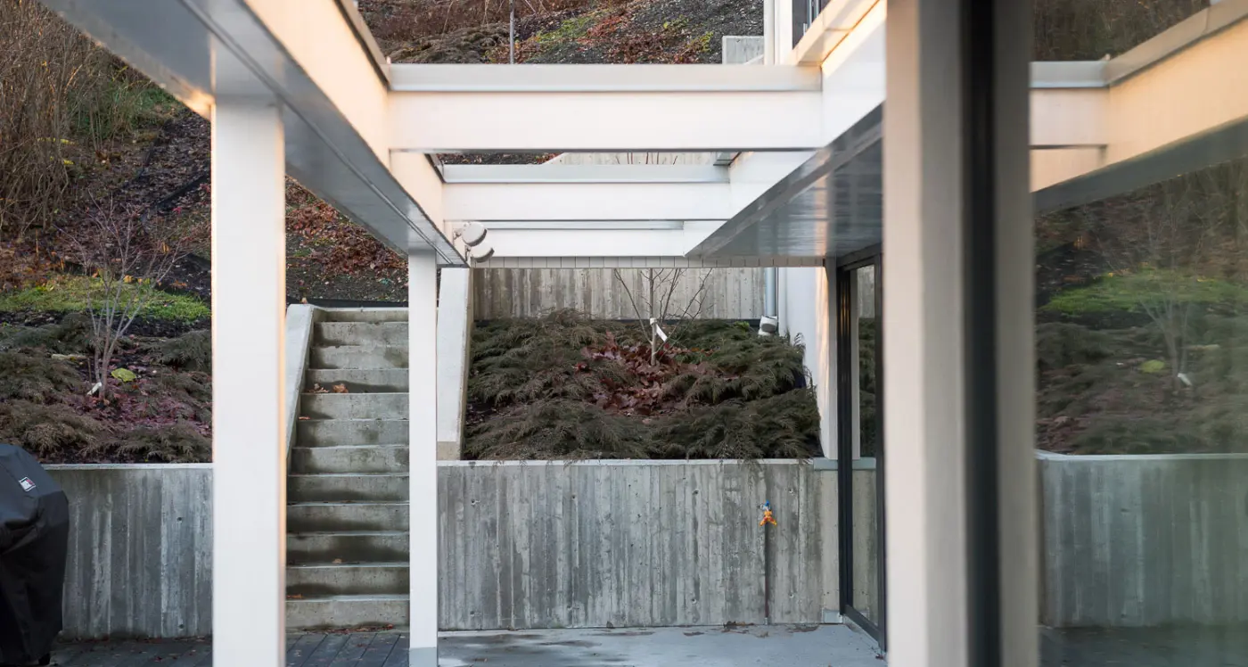 PLV17 — hvit pergola over uteplass, med murer i forskalingsbetong og trapp opp i hagen