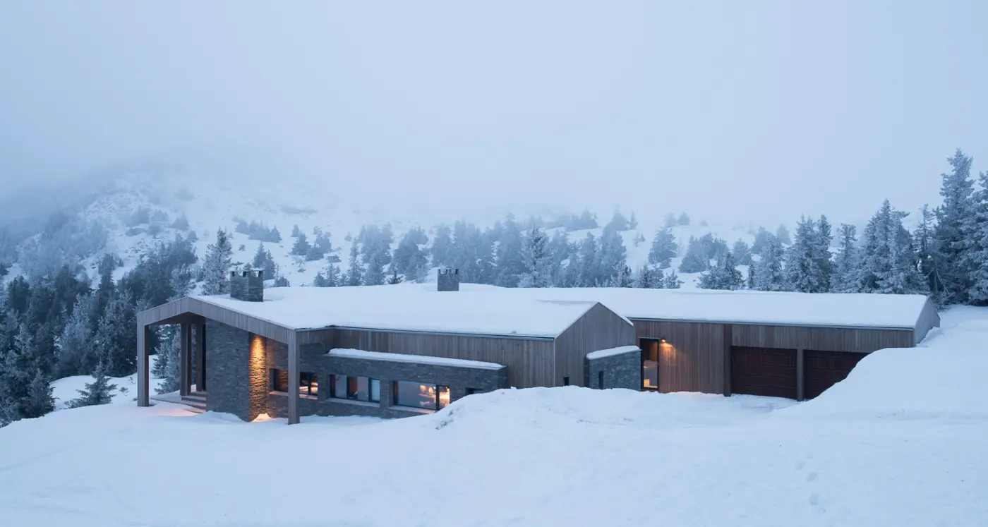KVF3 — lang lav hytte i tre og naturstein med garasjer, i snøkledd fjellandskap med tåke