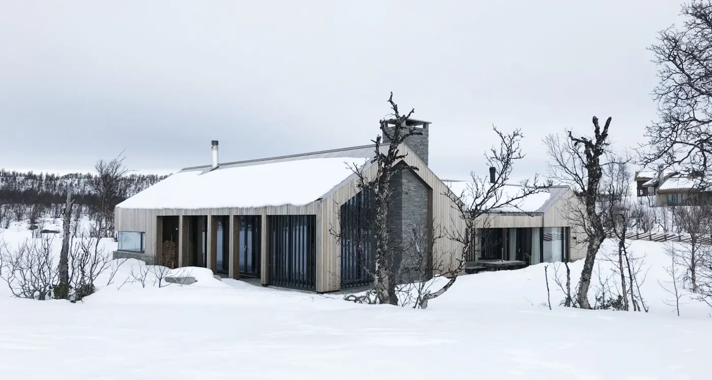 KIK2 — hytte i lys trekledning med natursteinspipe og spilefelt, snødekt på fjellet