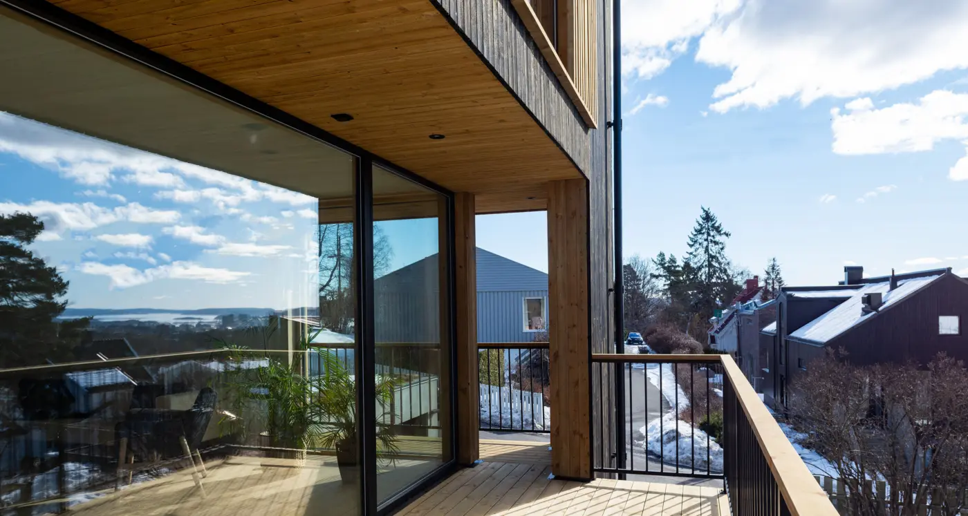 TÅS — balkong i tre med skyvedør i glass og utsikt over fjorden, med nabohusene nedenfor