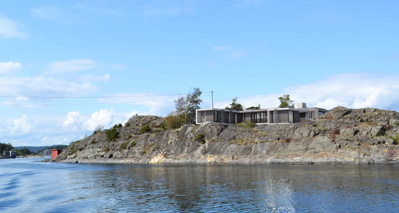 OST — lav bolig med flatt tak på svaberg, sett fra sjøen i skjærgården