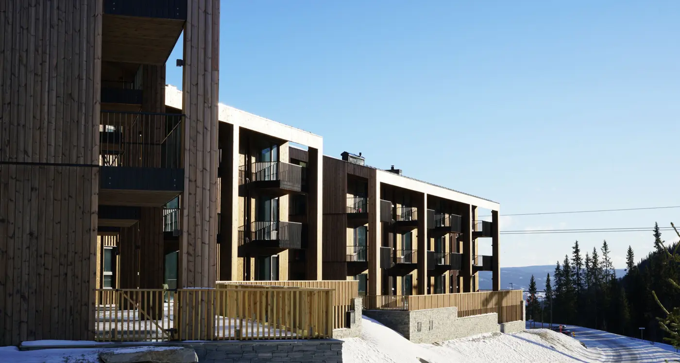 YSV — leilighetsbygg i lys trekledning med balkonger over natursteinsmur, med utsikt over dalen om vinteren