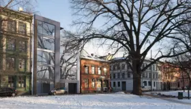 HEG42 — smalt nybygg i glass og metall innfelt mellom eldre bygårder, sett fra parken om vinteren