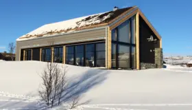 HOV — hytte med torvtak og glassfasade under høy gavl, med natursteinsmur, på snødekt fjell