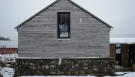 BAL — gavlvegg i grånet trekledning med høyt vindu, over natursteinsmur i snøvær