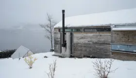 BAL — lang lav bolig i grånet tre med betongpipe og vindusbånd under takflaten, ved fjorden