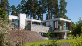 OEV6 — hvitpusset bolig i skrånende tomt med natursteinsmur og utkraget volum med treskjermer, under høye furuer