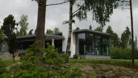 FÅG1 — hvit bolig med stort hjørnevindu og lavt tak, i furuskog med natursteinsmur