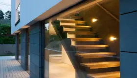 JOK10 — svevende eiketrapp sett gjennom glassfasaden i skumring, med skiferkledd vegg og terrasse