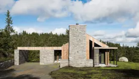 SJU — hytte i skifermur og lys trekledning med kraftig natursteinspipe, i granskog