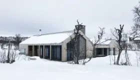 KIK2 — hytte i lys trekledning med natursteinspipe og spilefelt, snødekt på fjellet