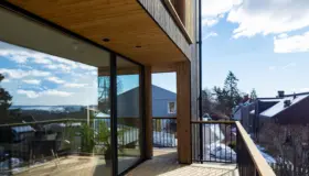 TÅS — balkong i tre med skyvedør i glass og utsikt over fjorden, med nabohusene nedenfor