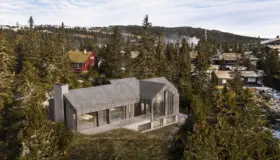 K81 — hytte i grå trekledning med spontak og høyt gavlvindu, sett ovenfra i hyttefelt