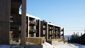 YSV — leilighetsbygg i lys trekledning med balkonger over natursteinsmur, med utsikt over dalen om vinteren