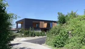 MÅN — bolig i mørk trekledning med utkraget overetasje og skyvbare treskjermer, over natursteinsmur