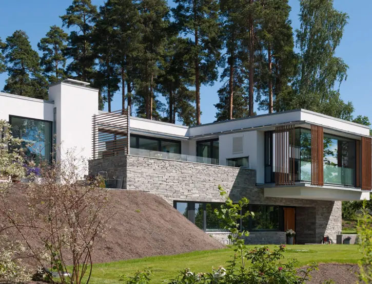OEV6 — hvitpusset bolig i skrånende tomt med natursteinsmur og utkraget volum med treskjermer, under høye furuer