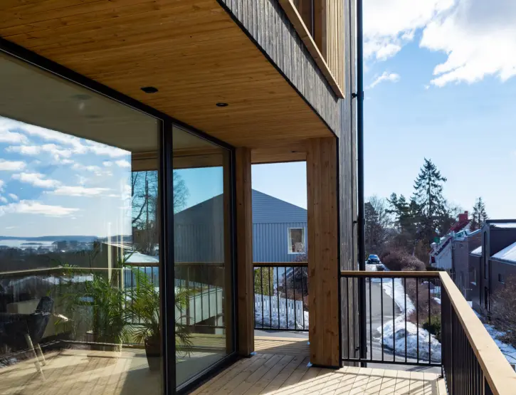 TÅS — balkong i tre med skyvedør i glass og utsikt over fjorden, med nabohusene nedenfor
