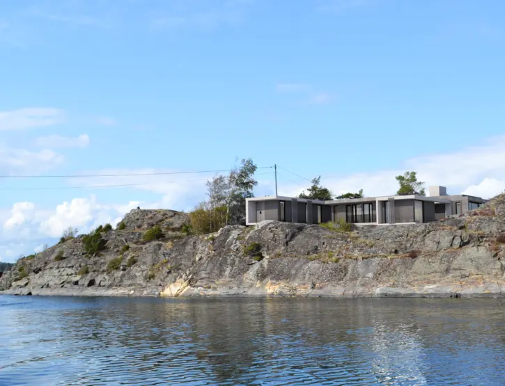 OST — lav bolig med flatt tak på svaberg, sett fra sjøen i skjærgården