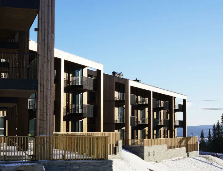 YSV — leilighetsbygg i lys trekledning med balkonger over natursteinsmur, med utsikt over dalen om vinteren