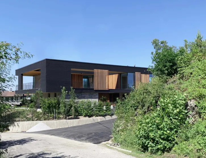 MÅN — bolig i mørk trekledning med utkraget overetasje og skyvbare treskjermer, over natursteinsmur