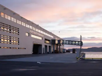 HRT — Hurtigruteterminalen i lys tegl med gangbro til kai, fotografert i solnedgang