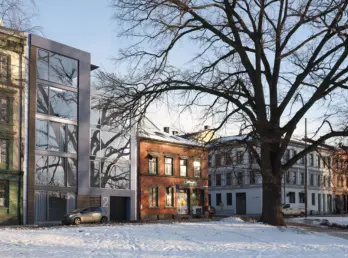 HEG42 — smalt nybygg i glass og metall innfelt mellom eldre bygårder, sett fra parken om vinteren