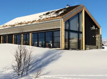 HOV — hytte med torvtak og glassfasade under høy gavl, med natursteinsmur, på snødekt fjell
