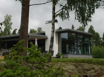 FÅG1 — hvit bolig med stort hjørnevindu og lavt tak, i furuskog med natursteinsmur