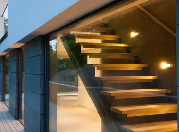 JOK10 — svevende eiketrapp sett gjennom glassfasaden i skumring, med skiferkledd vegg og terrasse