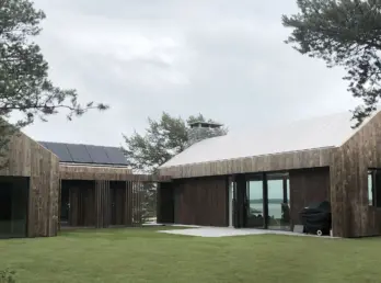 HUB — bolig i to gavlvolumer med mørk trekledning og solcellepaneler, med utsikt mot sjøen