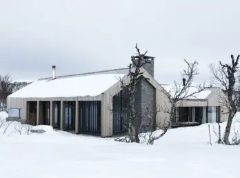 KIK2 — hytte i lys trekledning med natursteinspipe og spilefelt, snødekt på fjellet