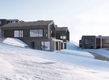NOR180 — hytter i grå trekledning som trappes ned den snødekte fjellsiden, med natursteinsmurer. Illustrasjon