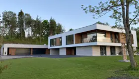 DNV3 — bolig med hvit overetasje over base i lys naturstein, med garasjerekke og skulptur på plenen