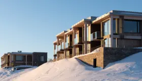 ØNS — leilighetsbygg med trekonstruksjon og glassbalkonger over natursteinsmur, i kveldssol og snø