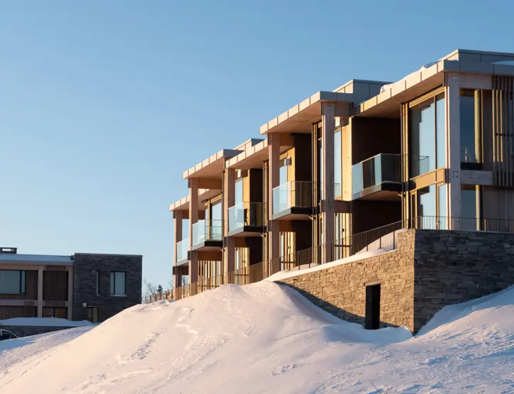 ØNS — leilighetsbygg med trekonstruksjon og glassbalkonger over natursteinsmur, i kveldssol og snø